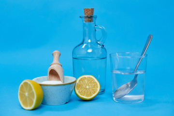 natural cleaning stuff, sustainability and eco living concept - lemon halves, washing soda, bottle of vinegar and glass with spoon over blue background