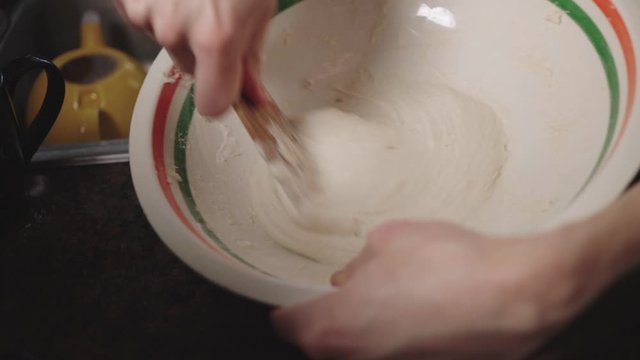Manual Method Of Mixing Dough In A Bowl Using A Wooden Spoon - Closeup Shot