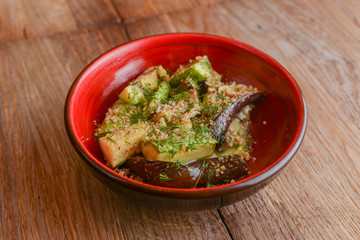 Backed eggplant with mozzarella cheese, tomatoes and basil served in a red bowl over rustic wooden table.