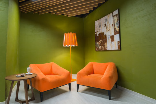 modern beautiful stylish interior two orange large armchairs in the lounge area with a modern lamp and a picture hanging on a green monophonic wall