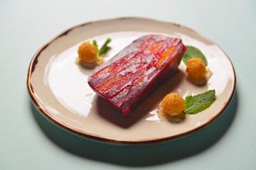 Red and pink layers of gelatin dessert served on a white plate over black wooden table.