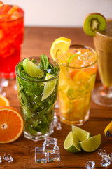Four tropical mixed drinks, orange, lemon and raspberries cocktails served on light wooden table.