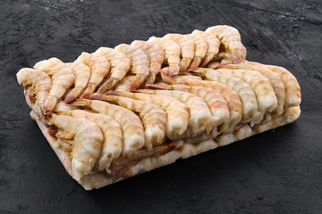 Raw tiger shrimp frozen in large ice cube on black background