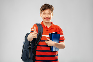 school, education and people concept - smiling student boy with backpack and books showing thumbs up over grey background