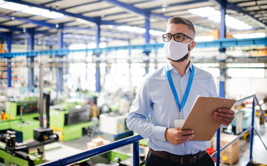 Technician or engineer with protective mask working in industrial factory, standing.