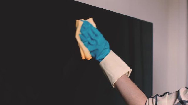 young woman in gloves with a rag wipes the plasma TV in the bedroom. Domestic Cleaning Service in home.