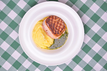 Filet mignon with mashed potatoes and pesto sauce served in a white plate over green plaid...