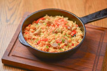 Rice with meat and vegetables served in a frying pan on wooden board over light rustic wooden table