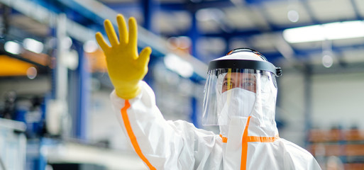 Worker with protective mask and suit in industrial factory, greeting hand gesture.