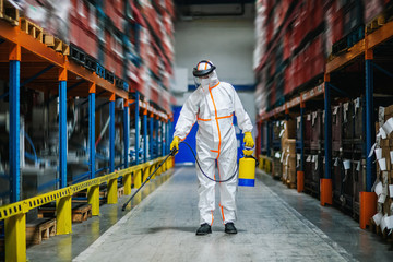 Man worker with protective mask and suit disinfecting industrial factory with spray gun. - Powered by Adobe