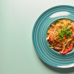 Plate of Asian chicken salad with rice noodles and sesame seeds served in a blue plate over blue mint background.