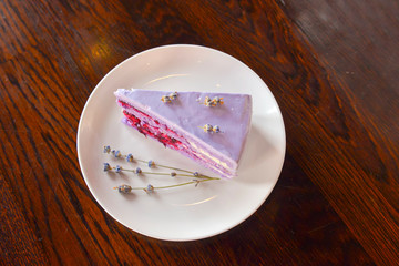 Slice of purple lavender cake with berries served with lavender flowers on a white plate.