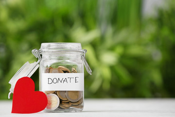 Jar with coins and red heart on table outdoors. Donation concept
