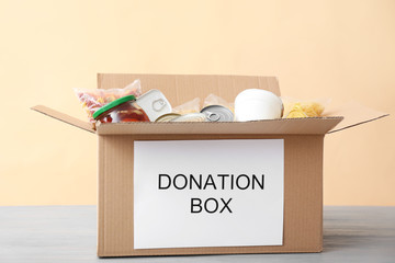 Box with donations on table against color background