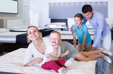 Obraz premium attractive young woman with husband and sons testing mattress in store