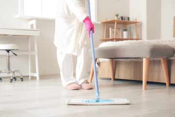 Housewife in protective costume cleaning floor in bedroom