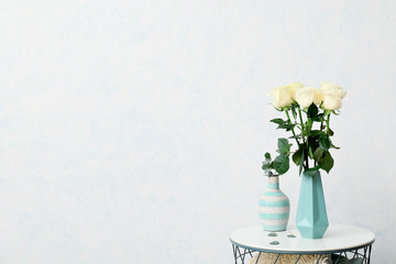 Vase with beautiful roses on table against light wall