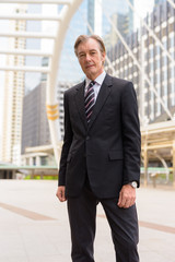 Mature handsome businessman in suit at skywalk bridge in the city