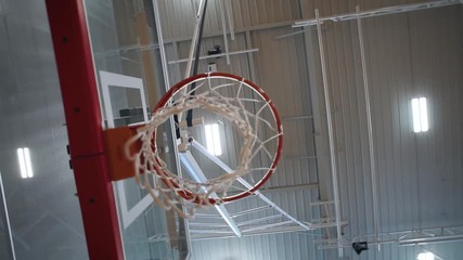 Looking up point of view spinning through white basketball net with red rim at an indoor gym