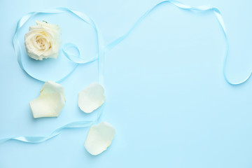 Beautiful white rose, petals and ribbon on color background