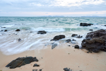 a wavy sea with rocks near a beach.