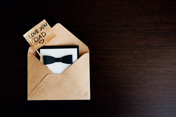 Greeting card with bow tie for father in craft envelope and piece of paper with text Love you Dad. Concept International Father's Day