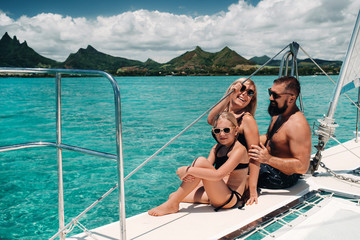a happy family in swimsuits sits on a catamaran in the Indian ocean. portrait of a family on a...