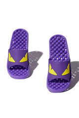 Detailed shot of violet massage sandals with knobby balls on the soles and with yellow eyes applique on straps. The pair of footwear for foot pain treatment is located on the white background. 