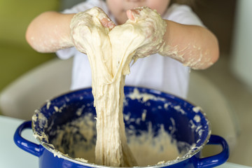 child kneads yeast dough in a blue pan, hands closeup.