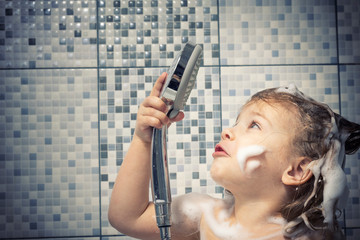 a little girl in foam is standing in the bathtub in her hand holding a shower and looking at him...