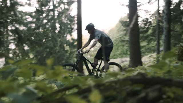 Amazing athletic mountain biker rushes along a road in a green forest. He is making some tricks.