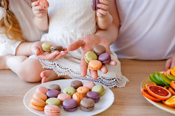 Family portrait of a happy mother, daughter and father posing in the kitchen during Breakfast, eating delicious macaroons, cakes, cookies. Married good relations, love each other