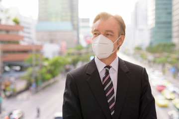 Face of mature businessman with mask thinking against view of the city