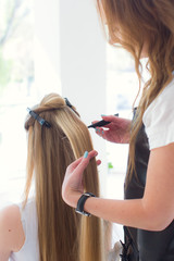 Fototapeta premium Stock Photo - Hairdresser smooths the hair of a client with a curling iron. Beautiful blonde girl in a beauty salon