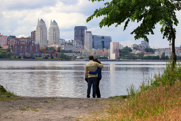 A young man and girl are standing and hugging on a cloudy morning on the background of Dnieper and...
