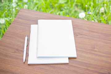 Clean and blank portrait magazine catalog and white pen on the wooden table with blurred green...