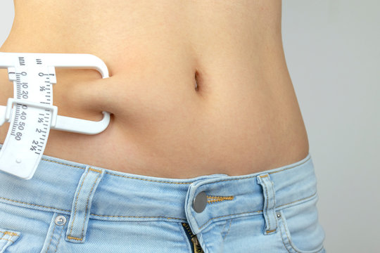 Body Fat Calipers, Woman Measuring Subcutaneous Percentage Of Fat On Her Belly. Young Woman Using Skinfold Calipers.