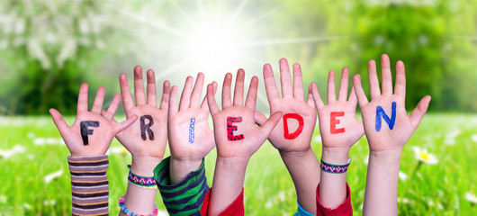 Children Hands Building Colorful German Word Frieden Means Peace. Sunny Green Grass Meadow As Background