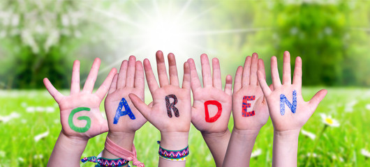 Children Hands Building Colorful English Word Garden. Sunny Green Grass Meadow As Background