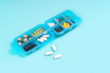 Prescription pills and vitamins in a blue pill box on blue color background. Flat lay photo, space for text.