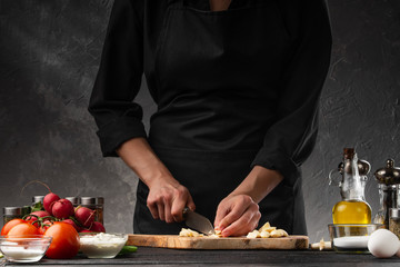 Chef chopping garlic for cooking. Against the background of a gray wall, and vegetables. Cooking and recipe book.