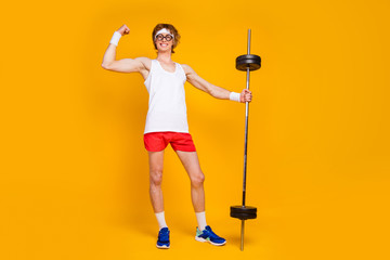 Full length body size view of his he nice attractive cheerful content slim sportive guy holding in hand barbell showing bicep work out isolated over bright vivid shine vibrant yellow color background