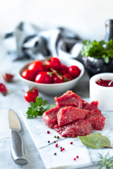 sliced fillet of raw fresh meat on a white marble background. Tomatoes, chili peppers and herbs for cooking. vertical