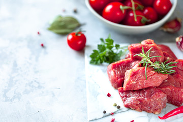 pieces of chopped raw fresh meat fillet on a white marble background. Tomatoes, chili peppers and herbs for cooking. Copy space
