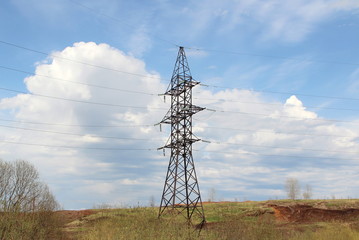 Iron pylon of a high voltage power line stands in a field against a blue sky.