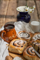 Basket of homemade buns with jam, served on old wooden table with walnuts and cup of milk