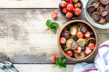 Tiny pancake cereal and chocolate mini pancakes in a wooden bowl with honey and strawberries on a wooden background. Top view. Copy space