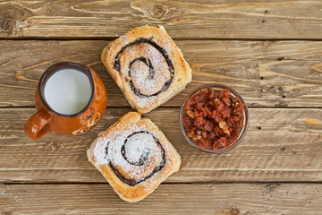 Basket of homemade buns with jam, served on old wooden table with cup of milk