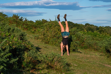Fototapeta premium Young girl in a hat doing a handstand on the green hill. Hiking and sport lifestyle concept.