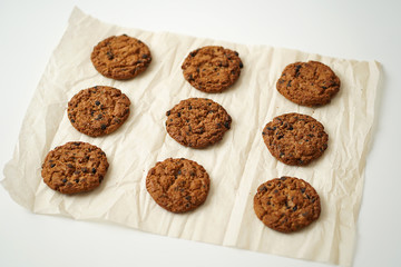 oatmeal round cookies with chocolate chips are spread out on parchment paper, on a white table, after baking